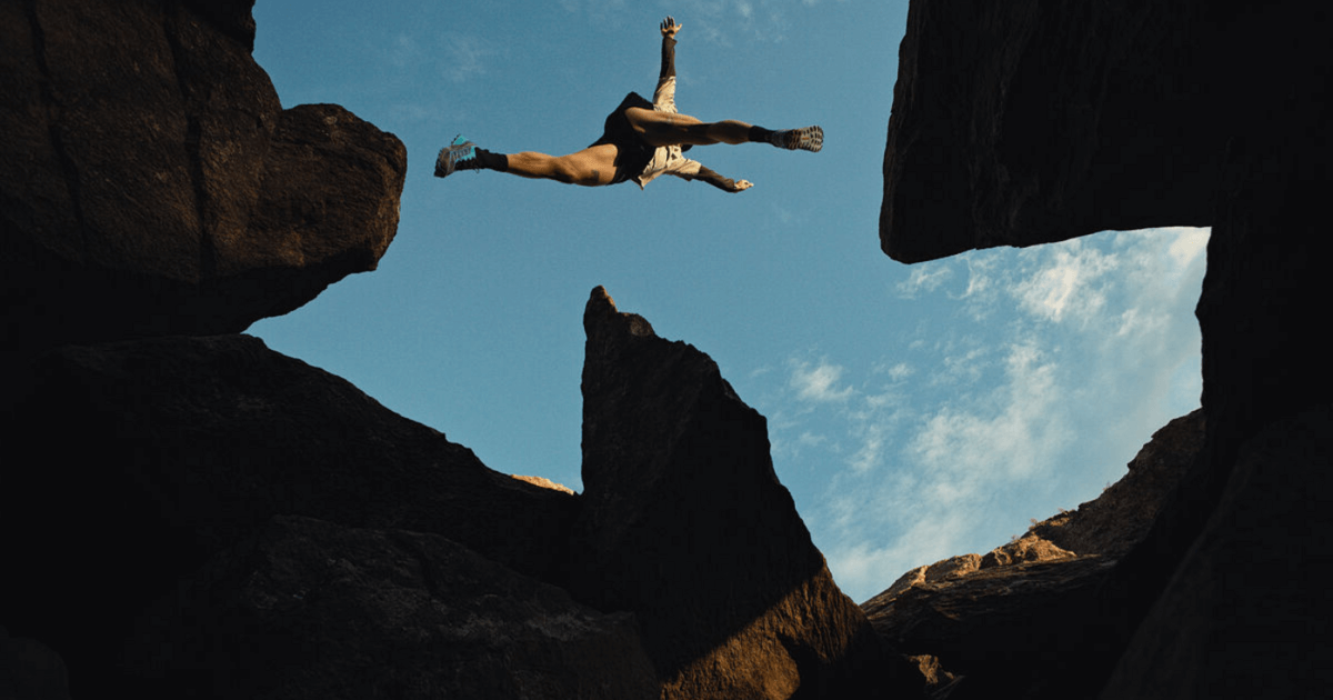 Mann springt über zwei Klippen mit Scarpa Outdoor Schuhen – dynamisches Outdoor Equipment im Einsatz