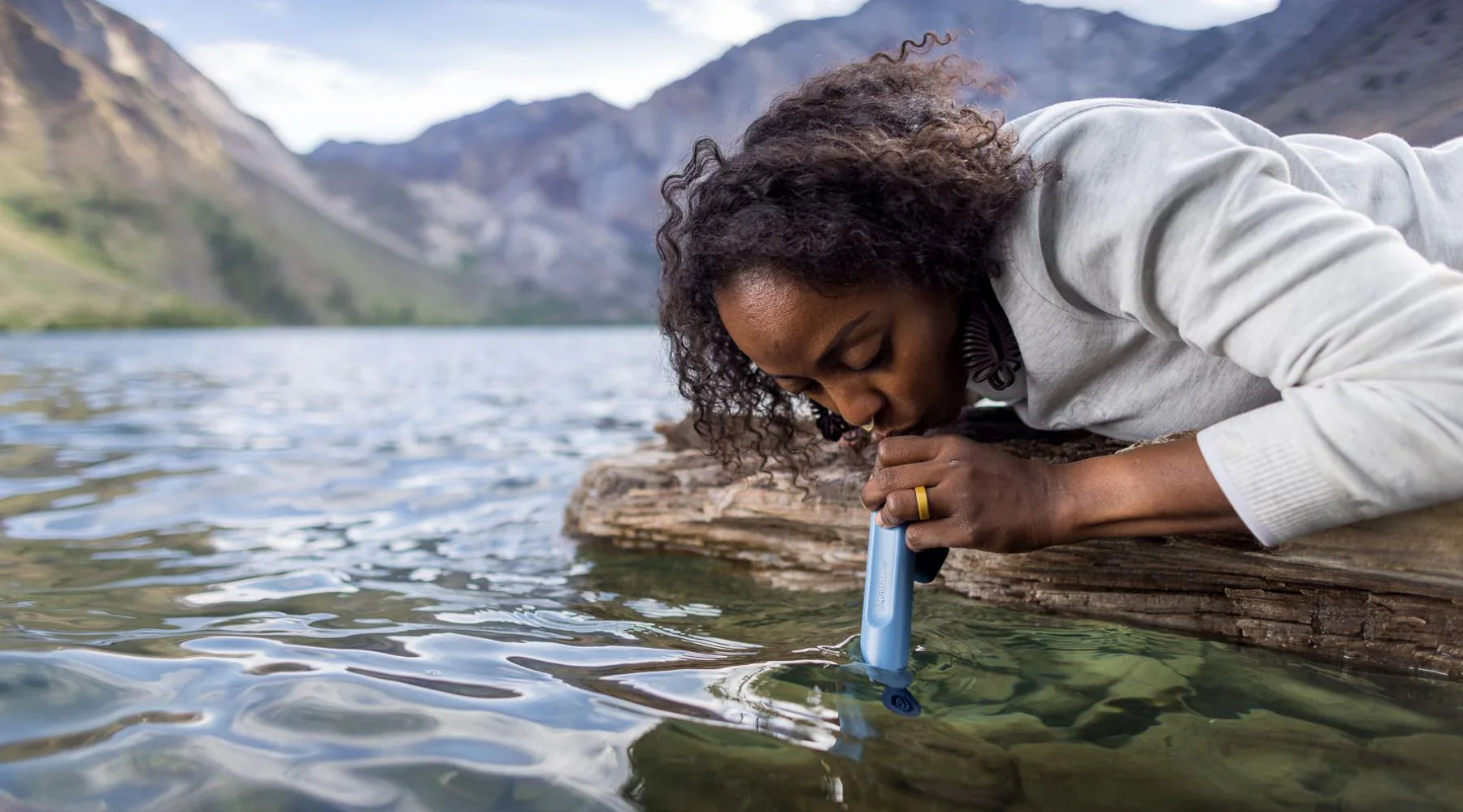 Eine Dame trinkt aus einem See mit ihrem LifeStraw Wasserfilter