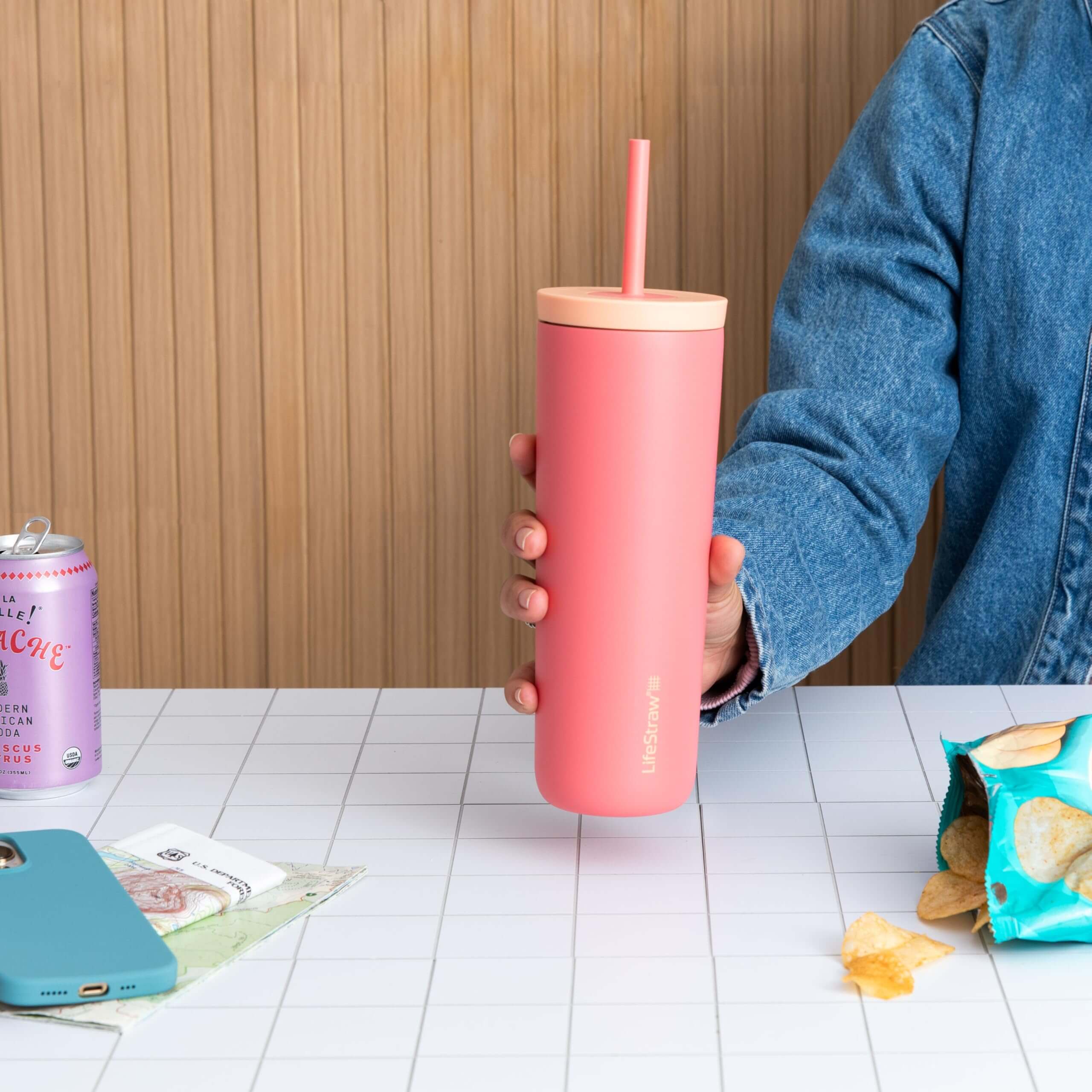 Der LifeStraw Tumbler in der Farbe Apricot im Einsatz - eine Dame hält den LifeStraw Tumbler, man sieht einen Tisch und Snacks
