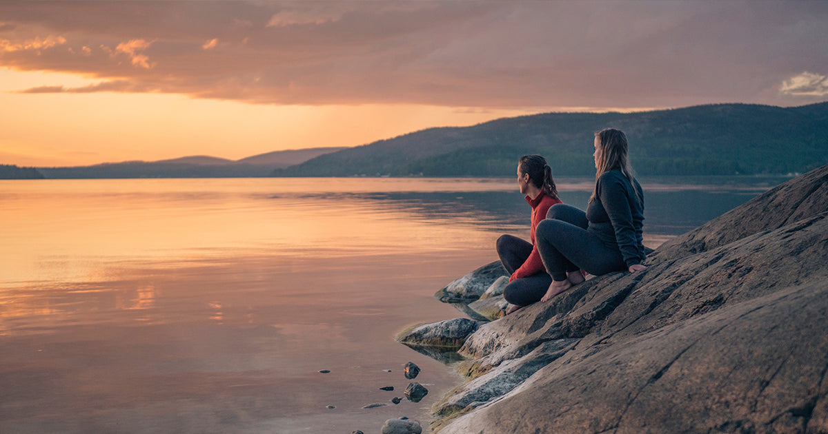 Outdoor Bekleidung Damen, Pärchen sitzt am Wasser zum Sonnenuntergang
